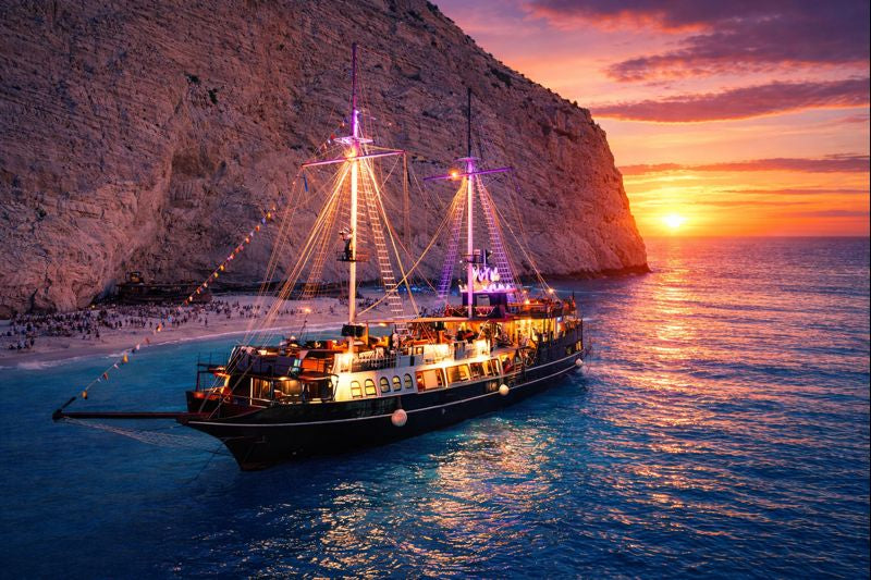 Sailing ship at sunset near a rocky coastline